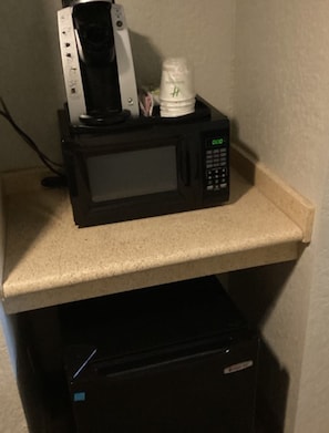 A microwave on a countertop with a coffee maker and a white cup on top.