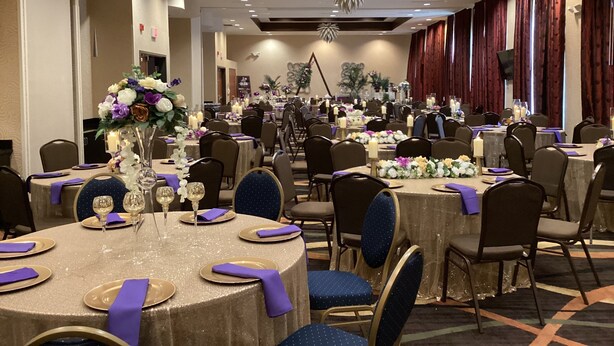 Uma sala de banquetes com mesas redondas, cadeiras e arranjos florais.