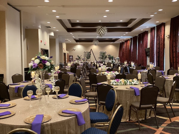 A banquet hall with round tables, chairs, and floral centerpieces.