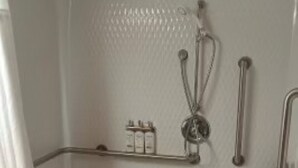 Casa de banho com chuveiro, barras de apoio e um espaço para produtos de higiene pessoal.