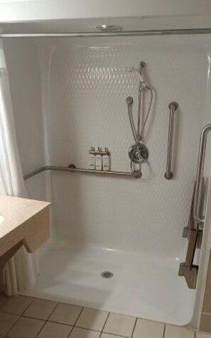 A bathroom with a shower, grab bars, and a shelf with toiletries.