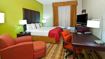 A hotel room with a bed, two chairs, a desk, a TV, and a window with curtains.