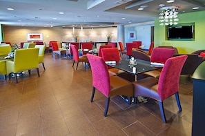 Un espace repas moderne doté de plusieurs tables et chaises, d’un téléviseur à écran plat fixé au mur et d’un plafond pourvu d’un éclairage encastré.