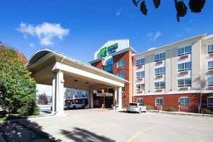 A hotel with a covered entrance, a sign for 'Hilton Express Suites', and a parking lot with cars.