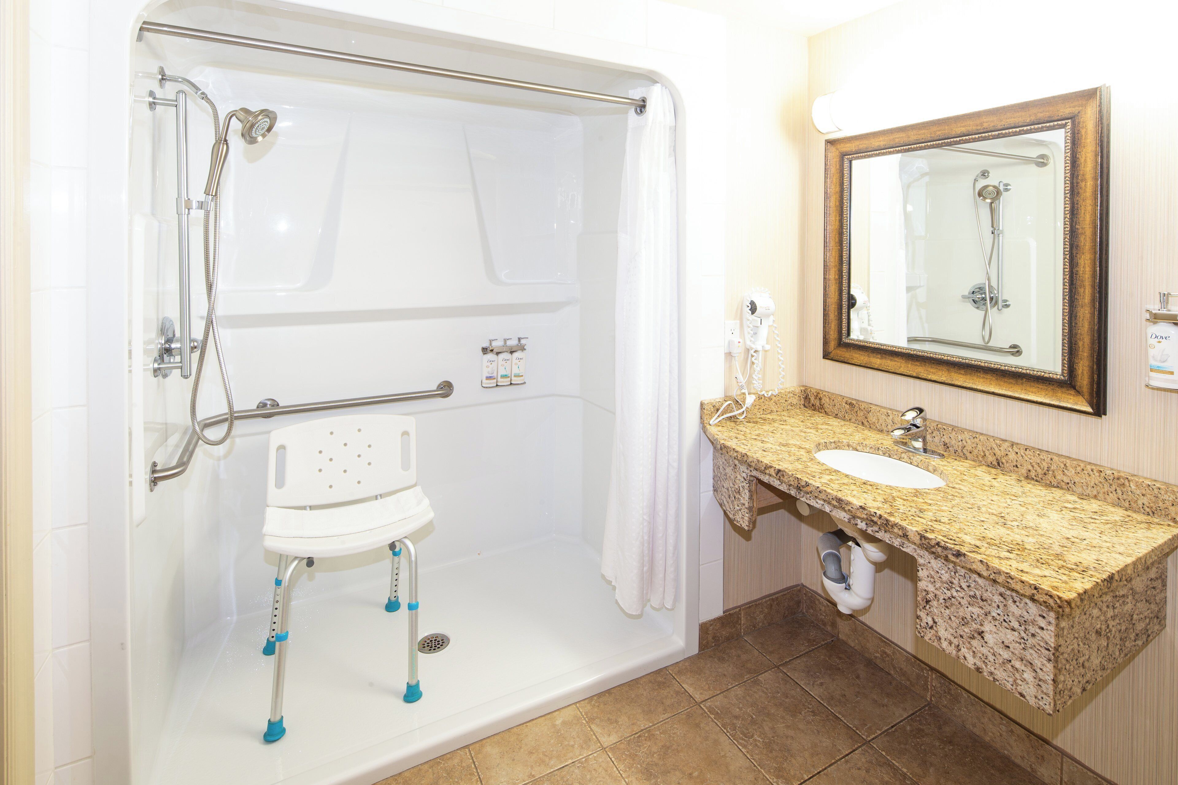 Une salle de bain dotée d’une douche à l’italienne, d’une barre d’appui et d’un lavabo avec un plan de travail en granit.