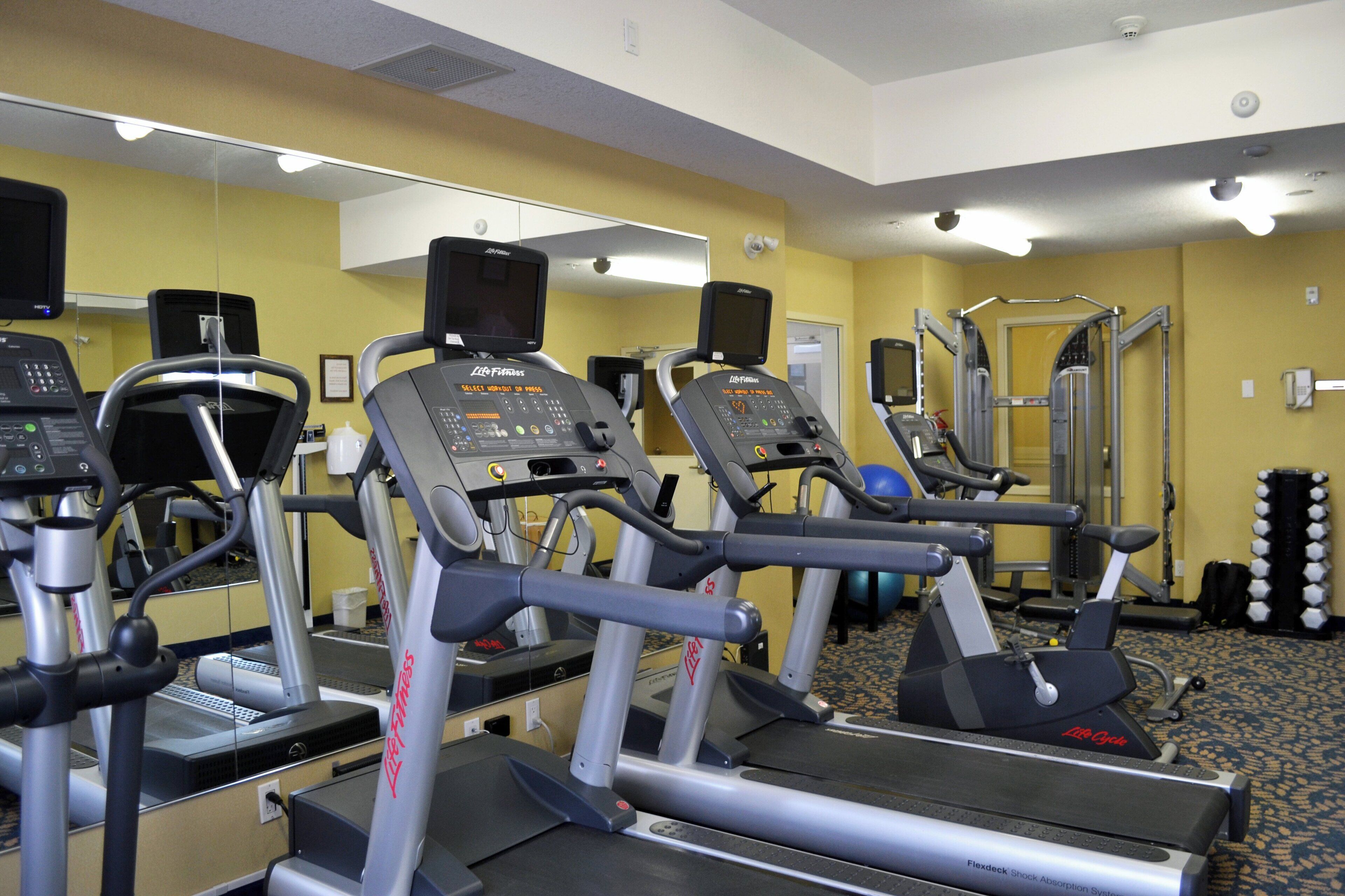 A gym with treadmills, a weight machine, and a mirrored wall.