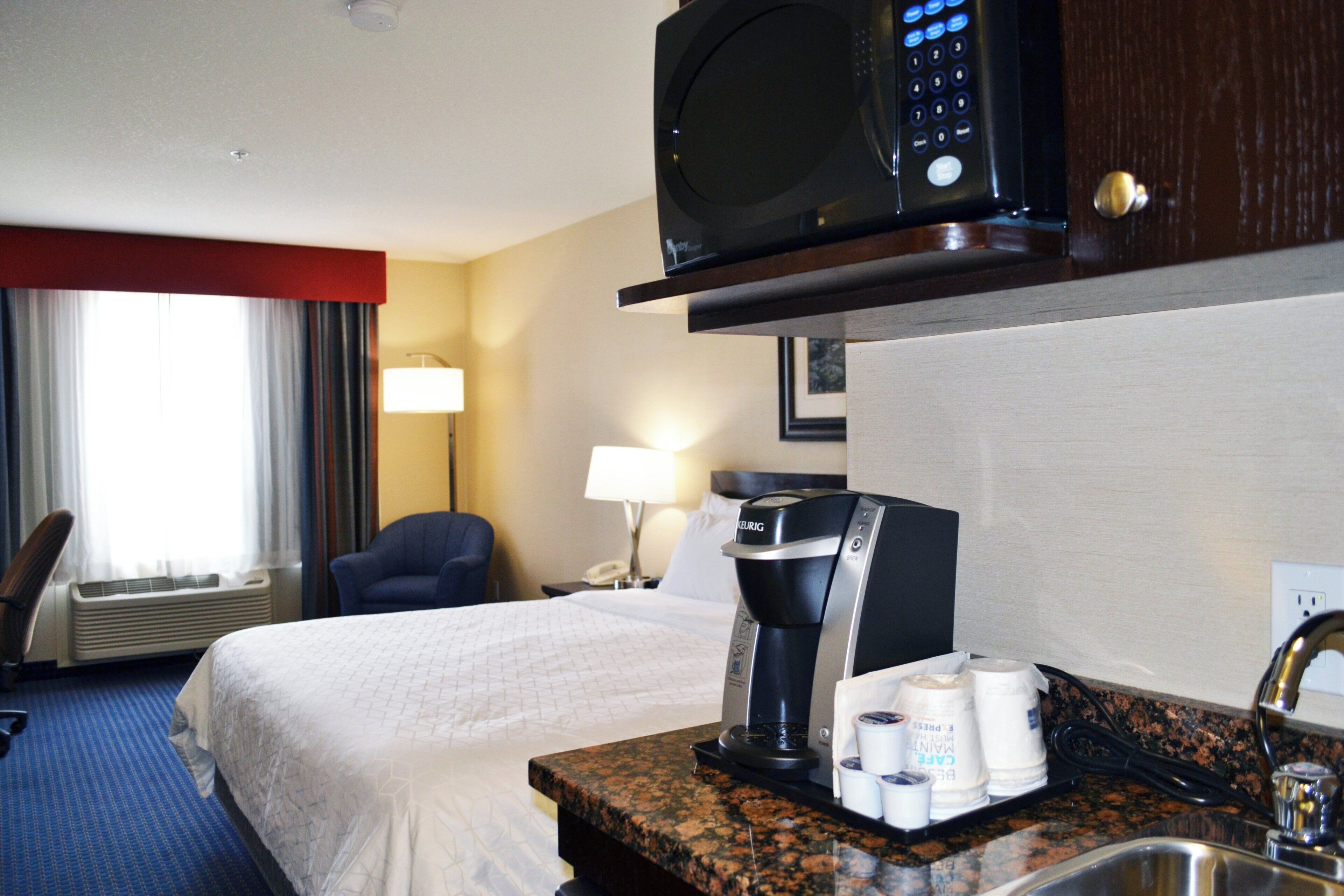 Una habitación de hotel con una cama, cafetera, microondas, escritorio y ventana con cortinas.
