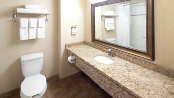 A bathroom with a toilet, two sinks, a large mirror, and a towel rack with multiple towels.