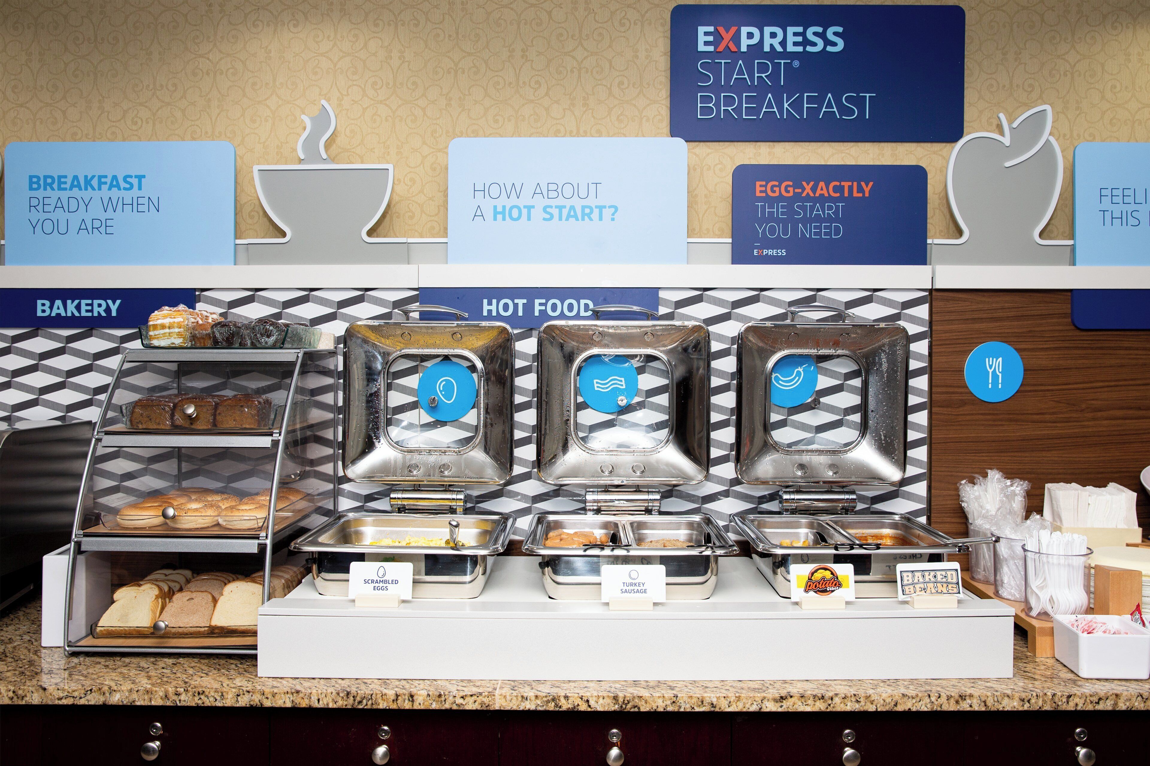 A breakfast buffet with labeled food stations including scrambled eggs, turkey sausage, and baked beans.