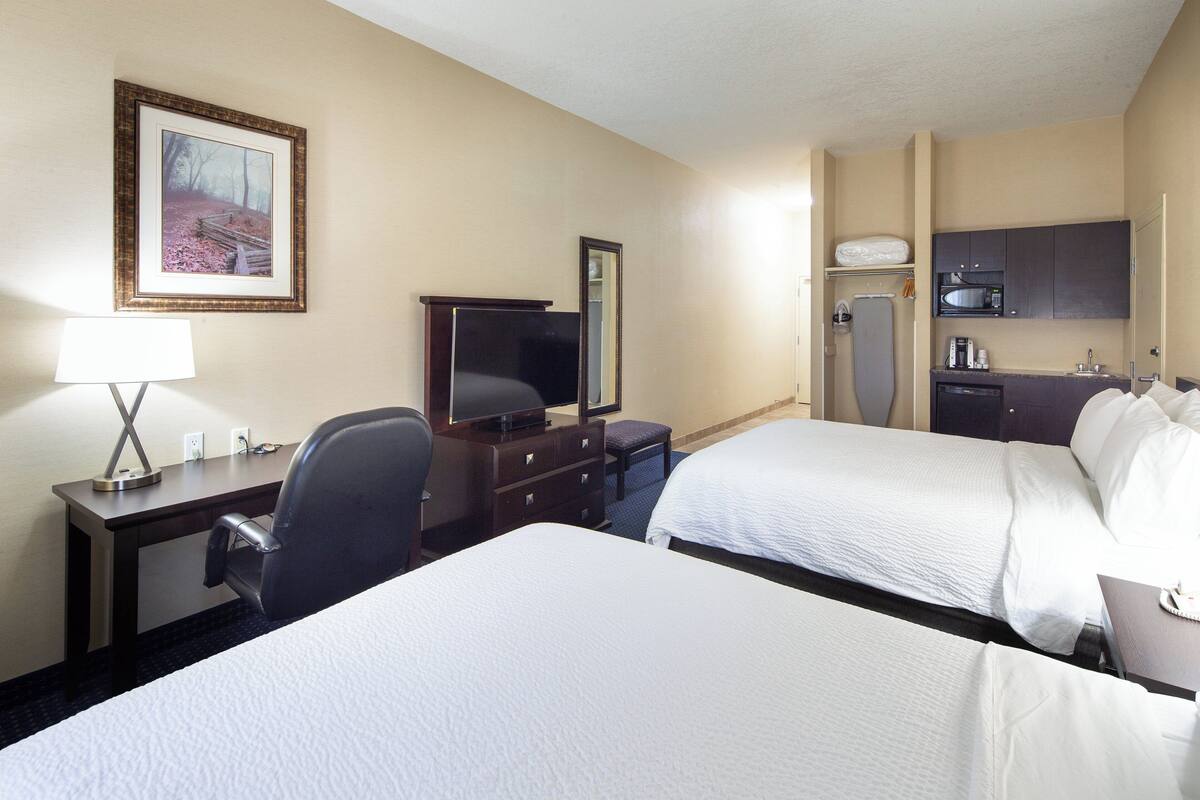 Ein Hotelzimmer mit zwei Betten, einem Schreibtisch mit Stuhl, einem Fernseher, einem Schminktisch und einer Minibar.