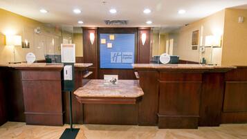 Un hall d’accueil d’hôtel avec des comptoirs en marbre, un panneau d’information central et une enseigne « Holiday Inn Express ».