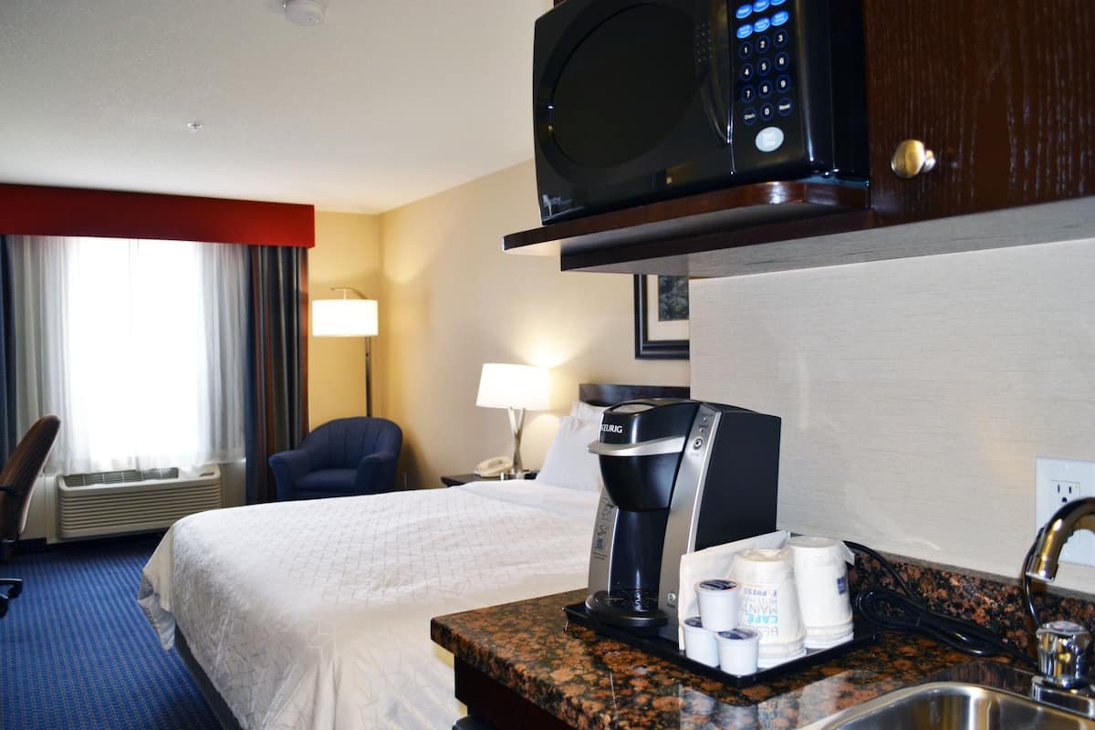 Ein Hotelzimmer mit einem Bett, einer Kaffeemaschine, einer Mikrowelle, einem Waschbecken und einem Sessel.