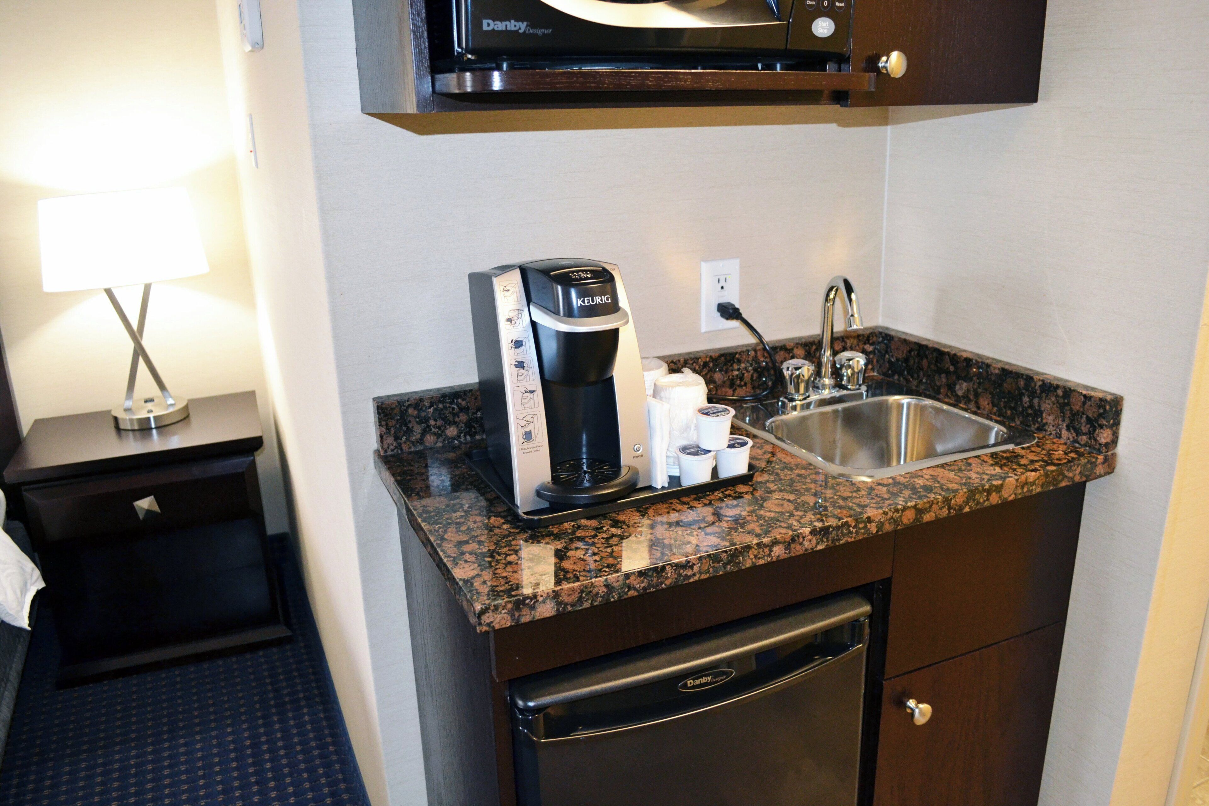 A compact kitchenette with a coffee maker, a sink, and a microwave above it.