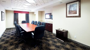 A conference room with a long table, multiple chairs, a small kitchenette, and a framed picture on the wall.