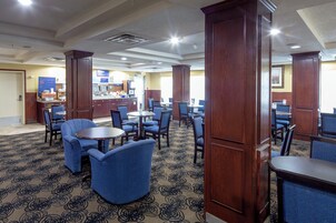 A hotel lobby with multiple seating areas, including round tables and blue chairs, and a reception desk in the background.