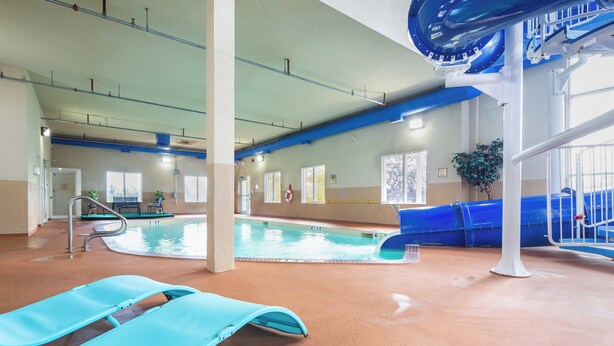 An indoor swimming pool with a blue slide, a lifeguard stand, and a pool ladder.