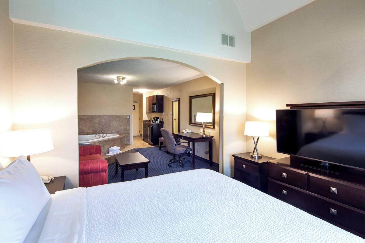 Ein Hotelzimmer mit Bett, Schreibtisch, Stuhl, Fernseher und einem durch einen Bogen sichtbaren Badezimmer.