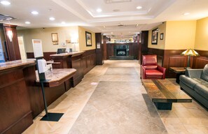 A hotel lobby with a reception desk, a fireplace, a red leather chair, and a sofa.