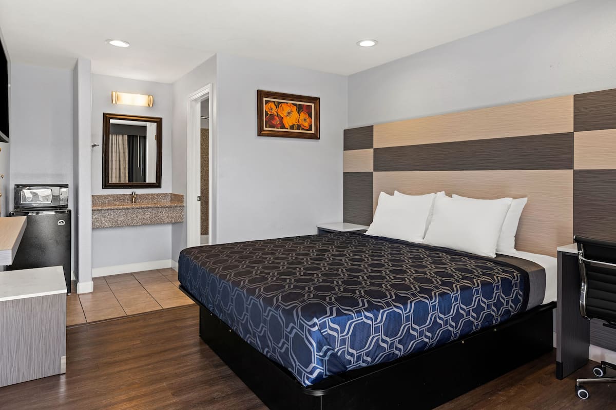 A modern hotel room with a large bed, a desk with a computer, and a bathroom with a mirror and towel rack.