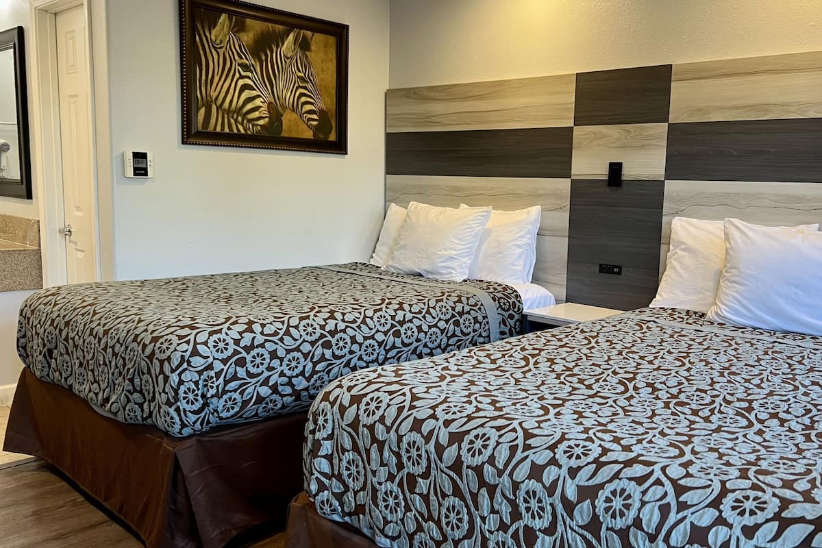 A hotel room with two beds, each with patterned bedding, a zebra painting on the wall, and a modern wood panel headboard.