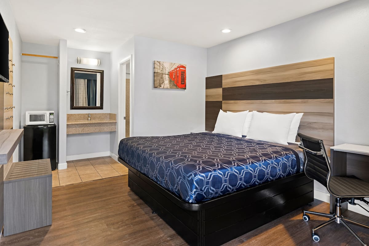 A modern hotel room with a large bed, a desk, a chair, a microwave, and a small trash bin.