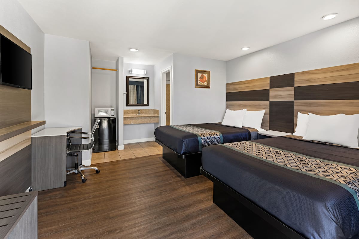 A hotel room with two beds, a desk, a chair, a TV, a microwave, and a trash bin.