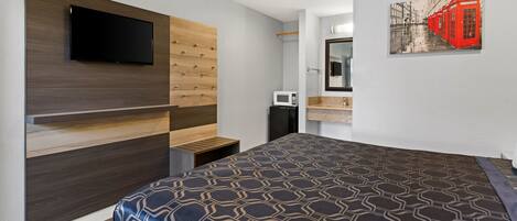Una habitación de hotel moderna con una cama grande, un televisor montado, un microondas y un baño con espejo y lavamanos.