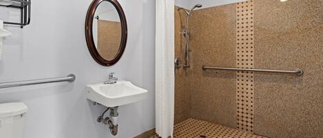 A bathroom with a toilet, sink, mirror, shower, and grab bars.