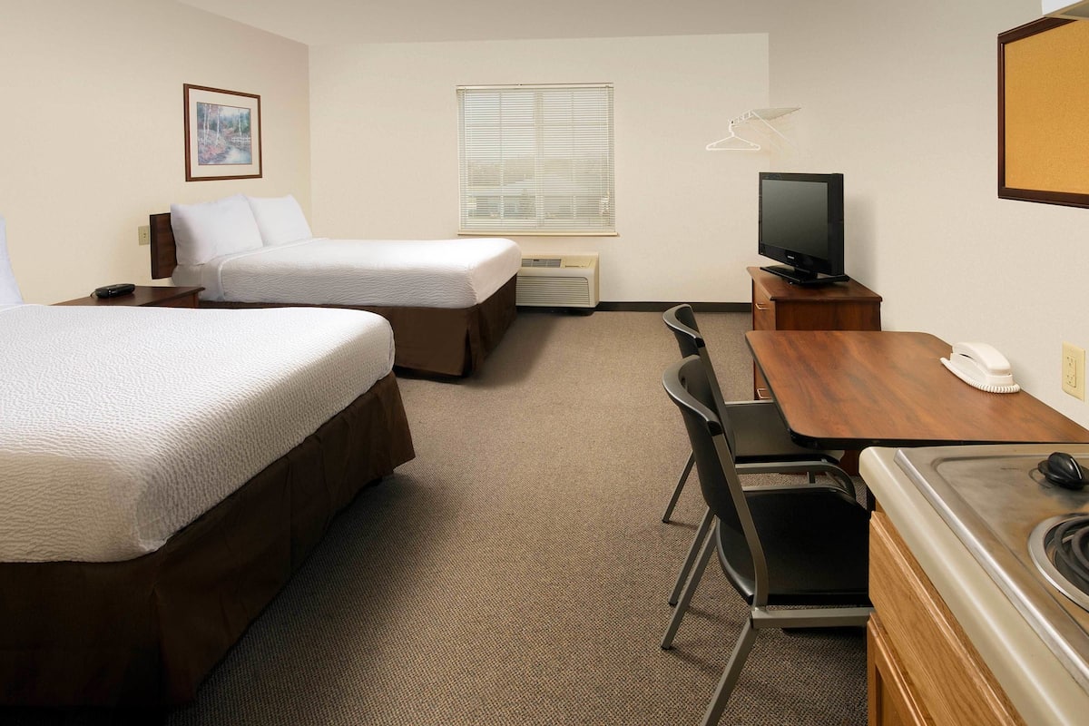 Ein Hotelzimmer mit zwei Betten, einem Schreibtisch, einem Fernseher und einer kleinen Küchenzeile.