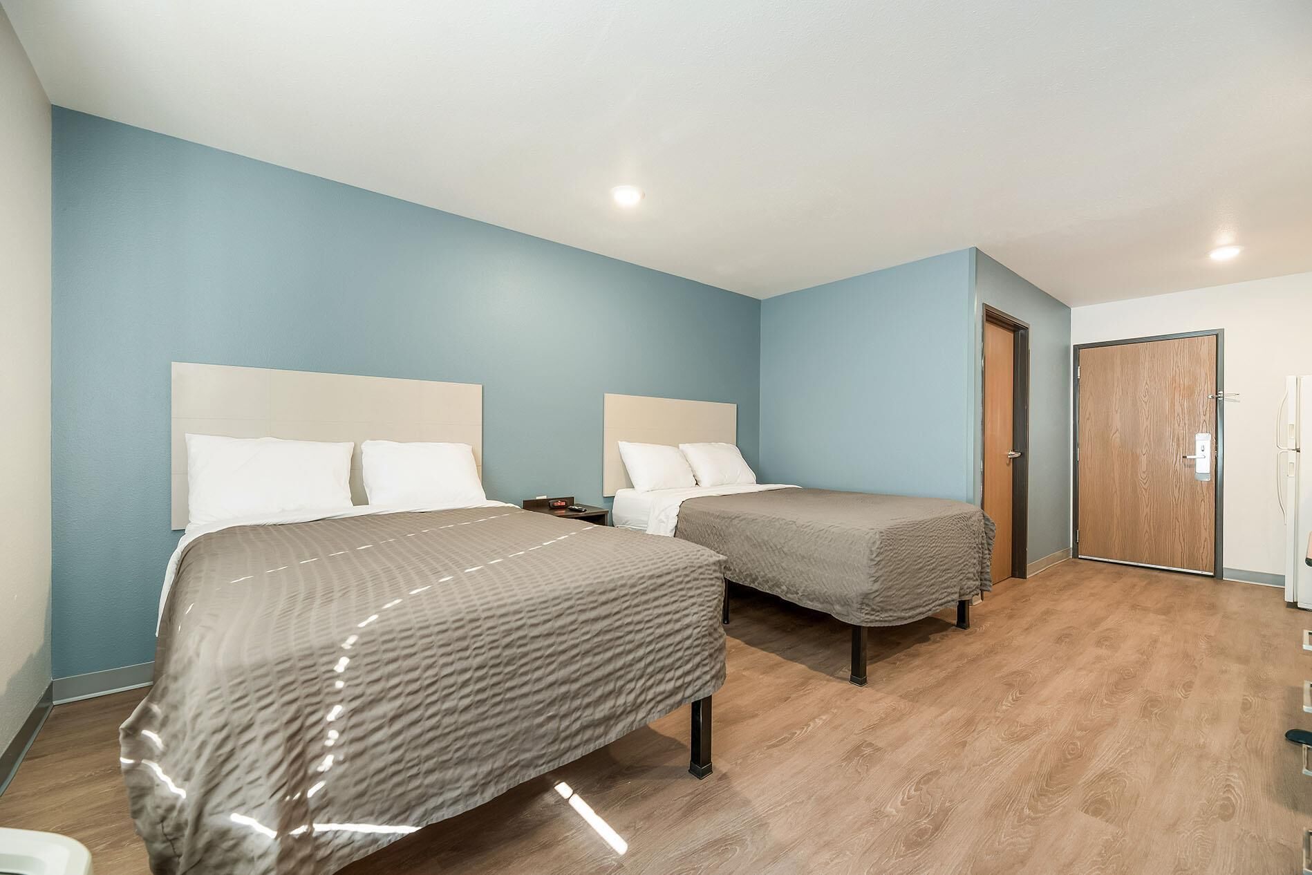 A hotel room with two beds, a wooden floor, and a door.