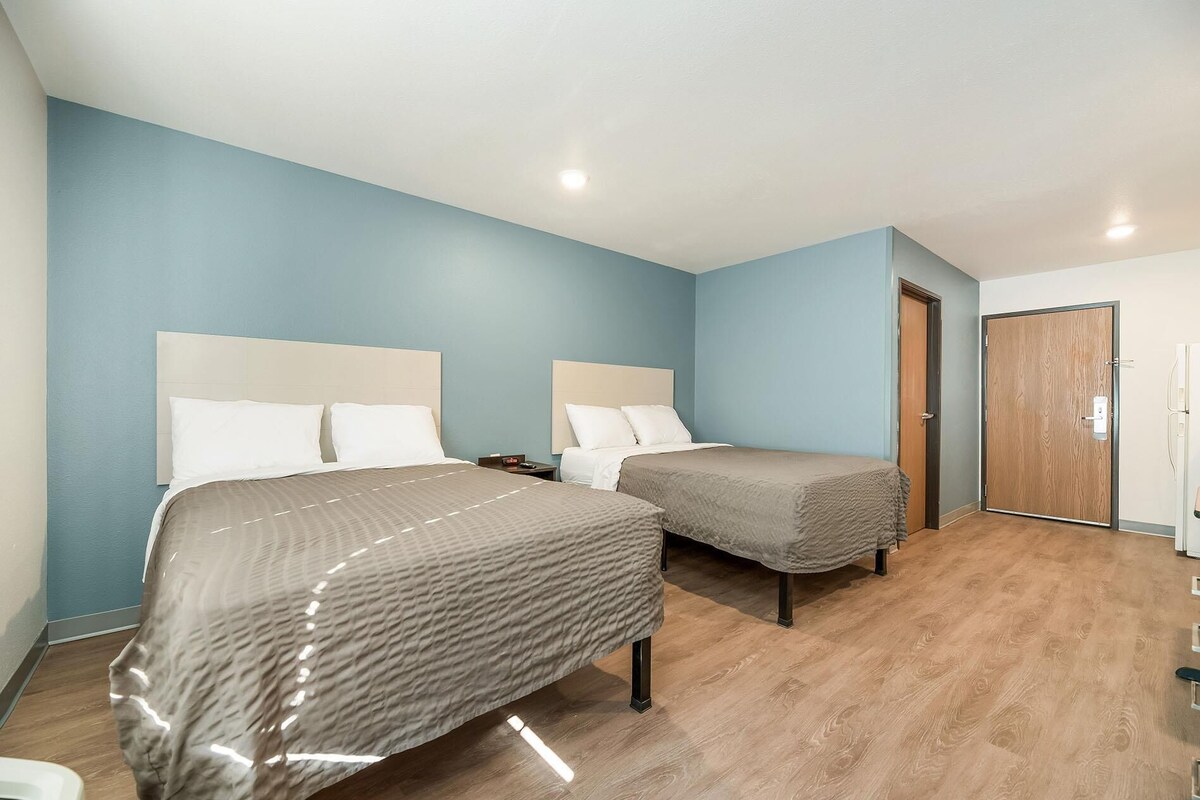 A hotel room with two beds, a wooden floor, and a door.
