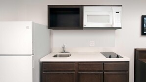 Una cocina compacta con un refrigerador blanco, un microondas, un lavamanos y gabinetes de madera oscura.