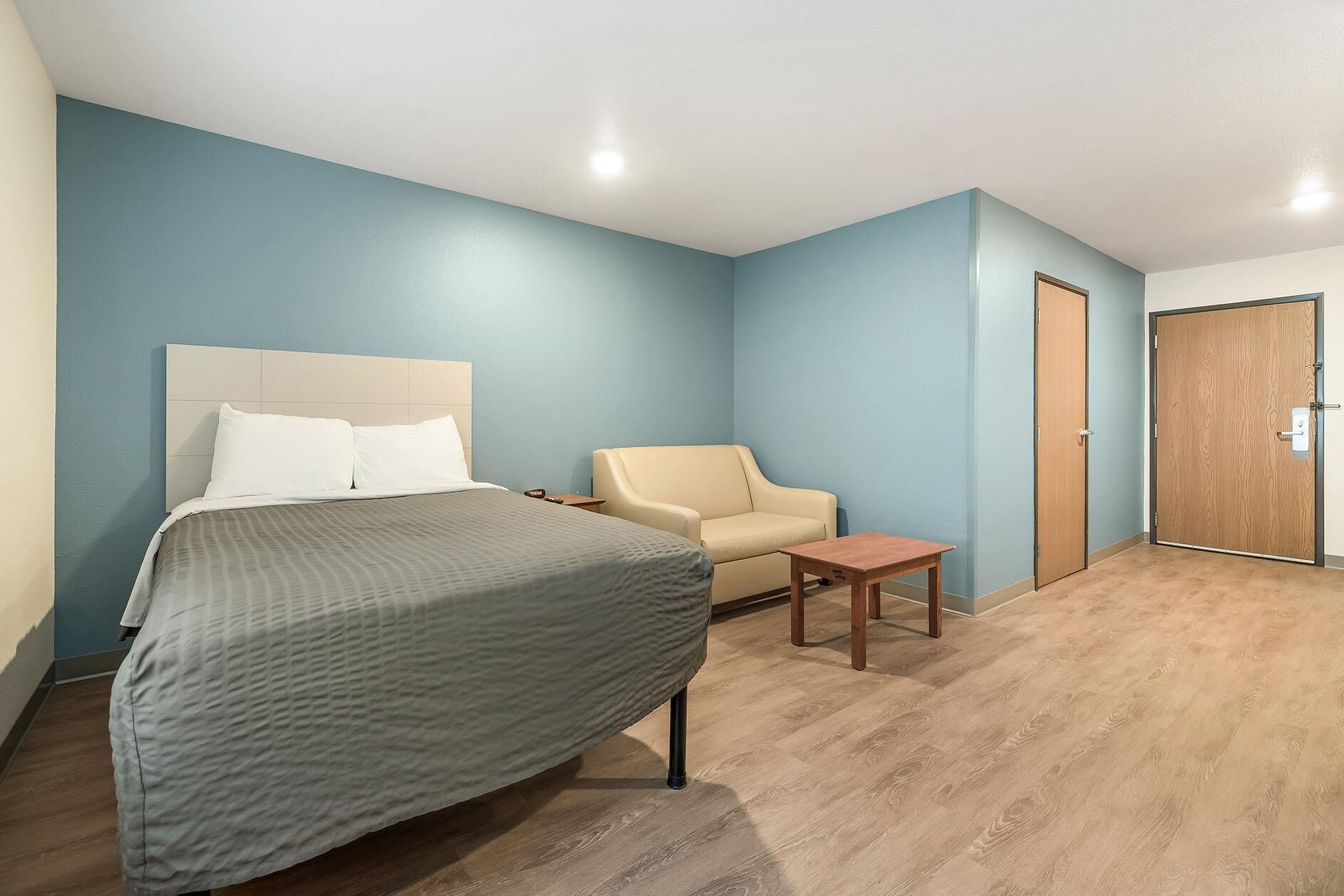 Una habitación de hotel con una cama, una silla, una mesita y una puerta.