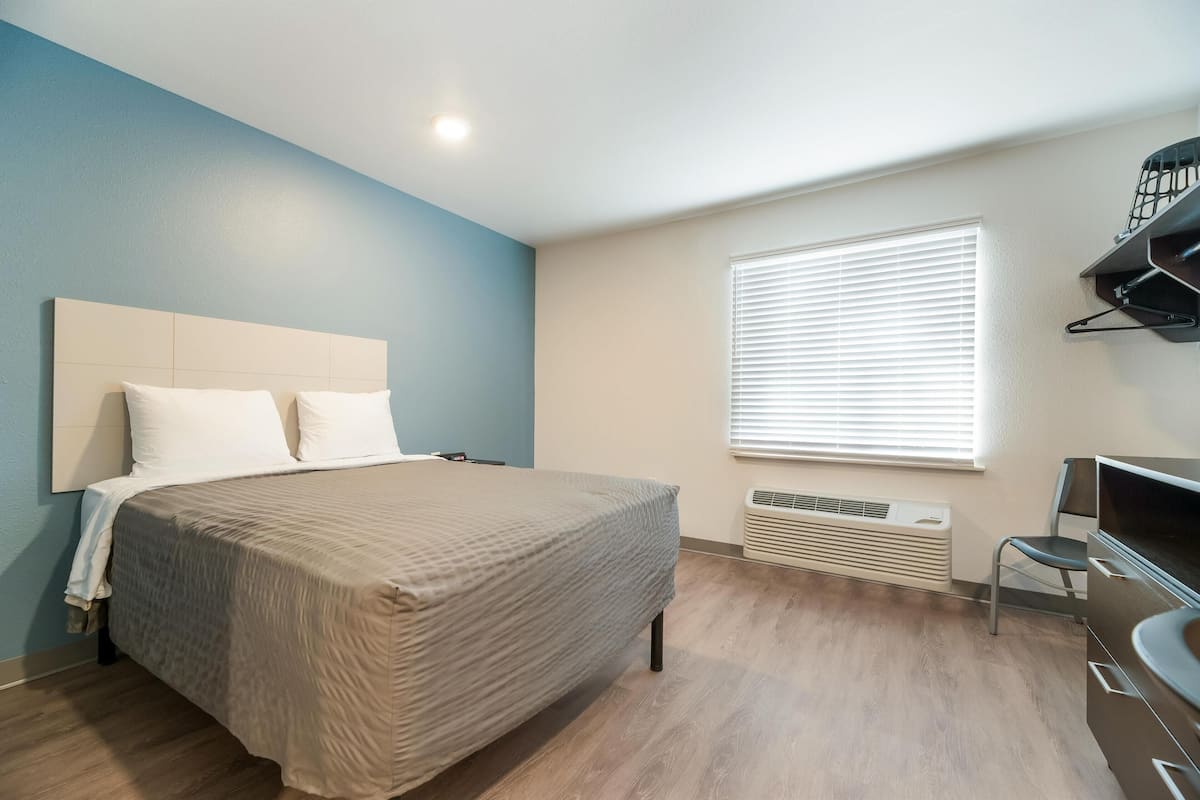 Ein Schlafzimmer mit Bett, Stuhl, Schreibtisch und einem Fenster mit Jalousien.