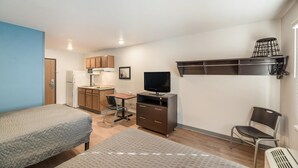 Una habitación pequeña con dos camas, un escritorio con computadora, televisor y kitchenette.