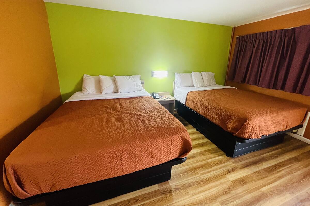 A hotel room with two beds, green walls, wooden flooring, and a window with curtains.
