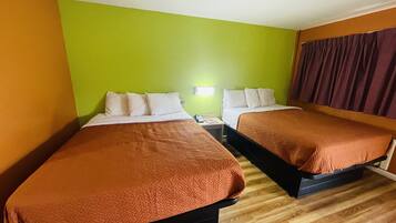 A hotel room with two beds, green walls, wooden flooring, and a window with curtains.