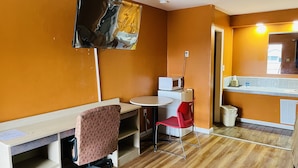 Une pièce avec un plancher en bois, un bureau avec une chaise, un four à micro-ondes et un grand tableau accroché au mur.
