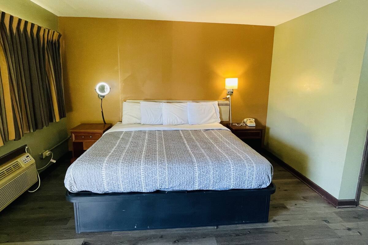 A hotel room with a bed, bedside lamps, a telephone, and a wall-mounted heater.