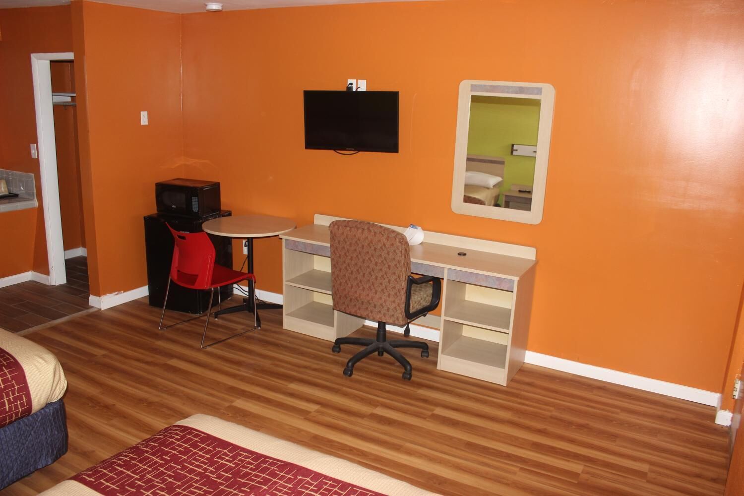 A room with orange walls, a wooden floor, a desk with a chair, a television, and a mirror.