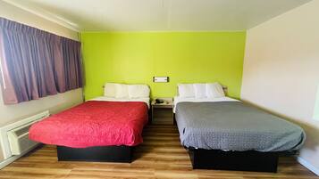 A room with two beds, each with a different colored bedspread, a nightstand with a phone and a remote, and a window with curtains.