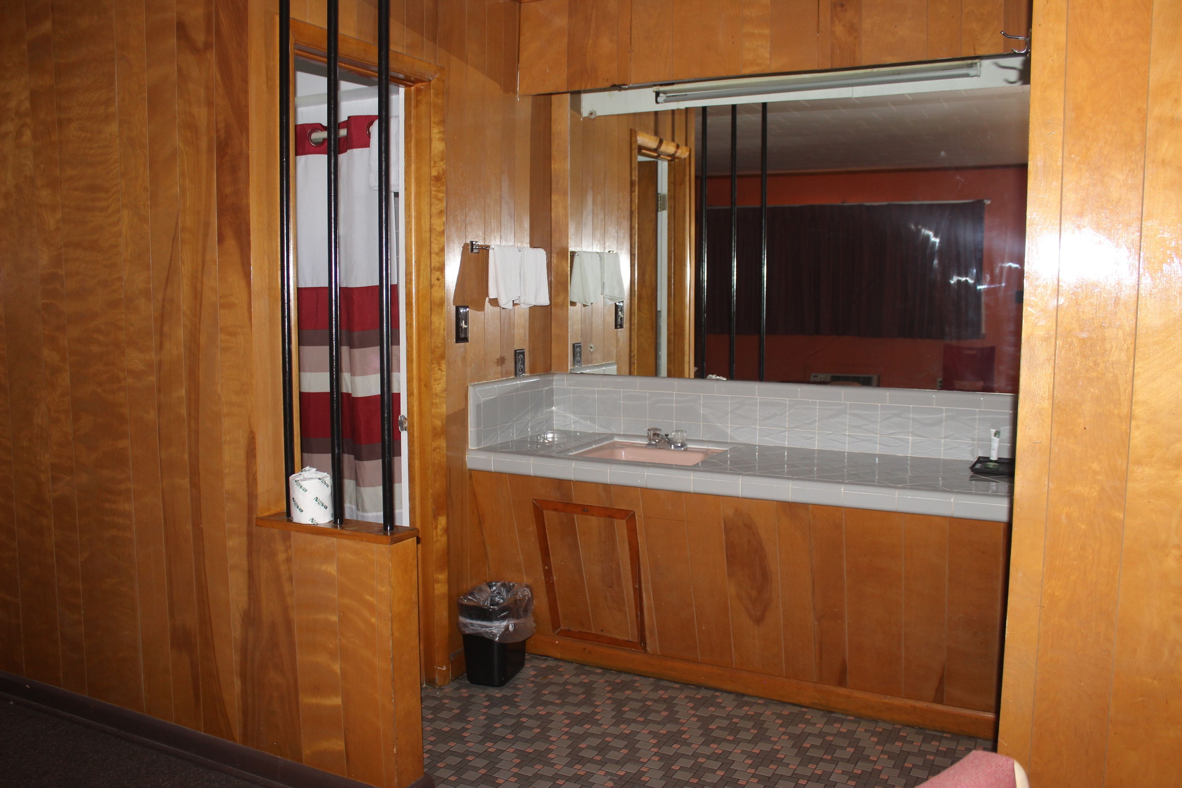 A wooden-paneled bathroom with a sink, mirror, and towel rack.