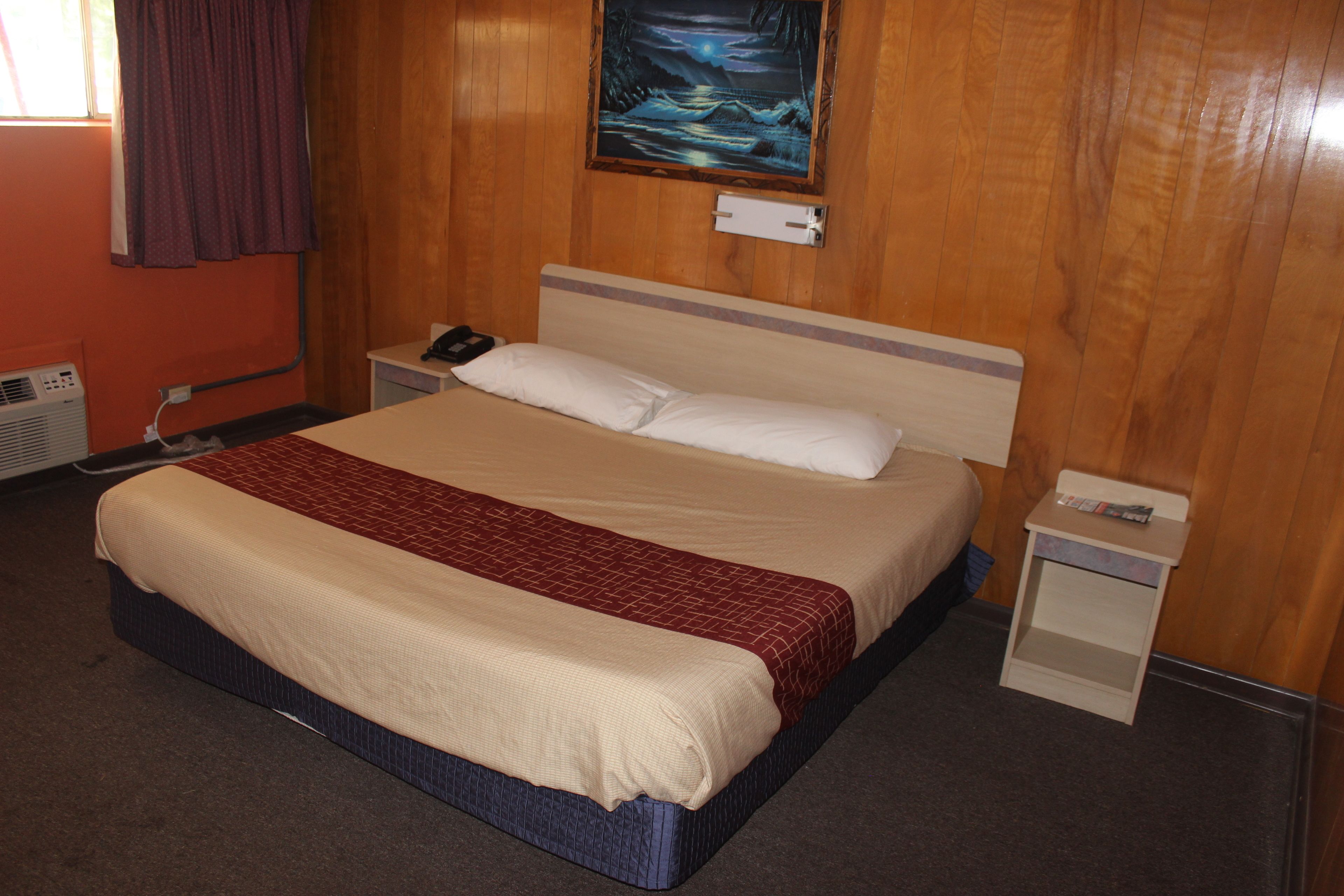 Habitación de hotel con cama, mesita de noche, teléfono en la pared, un cuadro y una ventana con cortinas.