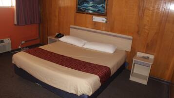 Habitación de hotel con cama, mesita de noche, teléfono en la pared, un cuadro y una ventana con cortinas.