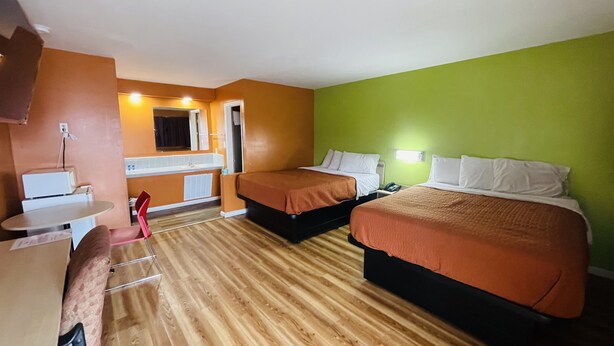 Une chambre d’hôtel avec deux lits, un bureau, une chaise, une petite table et un coin salle de bain.