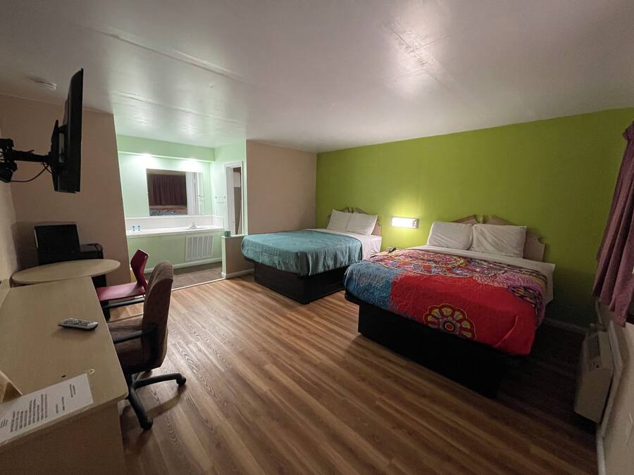 Habitación de hotel con dos camas, un escritorio con silla, una mesita y una ventana con vistas al baño.