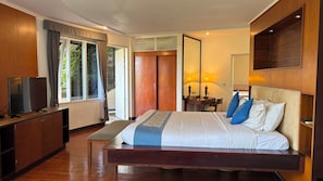A bedroom with a large bed, a TV, a desk, and a wardrobe.