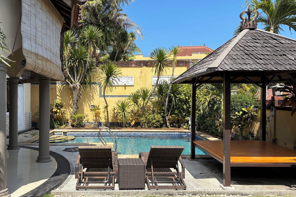 Un espace piscine aménagé avec des chaises longues, un gazebo et des plantes tropicales.