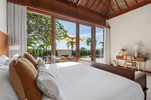 Ein geräumiges Schlafzimmer mit einem großen Bett, einem Schreibtisch und Blick auf Pool und Bäume.