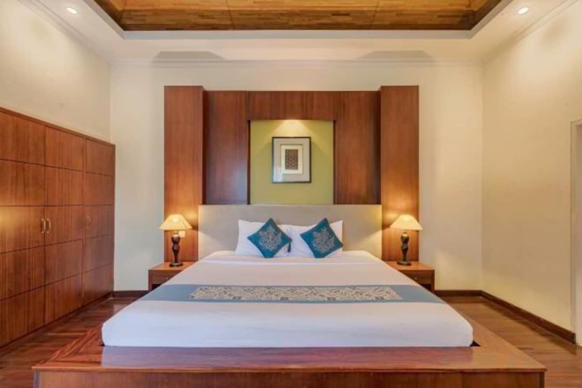 Habitación de hotel con una cama grande, cabecero de madera, dos lámparas de noche y un cuadro enmarcado sobre la cama.